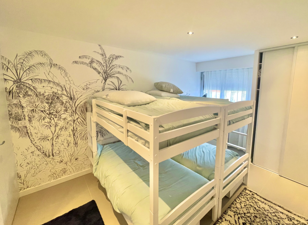 Aménagement intérieur d'un appartement de vacances cannois : chambre avec deux lits superposés et tapisserie murale motif palmiers
