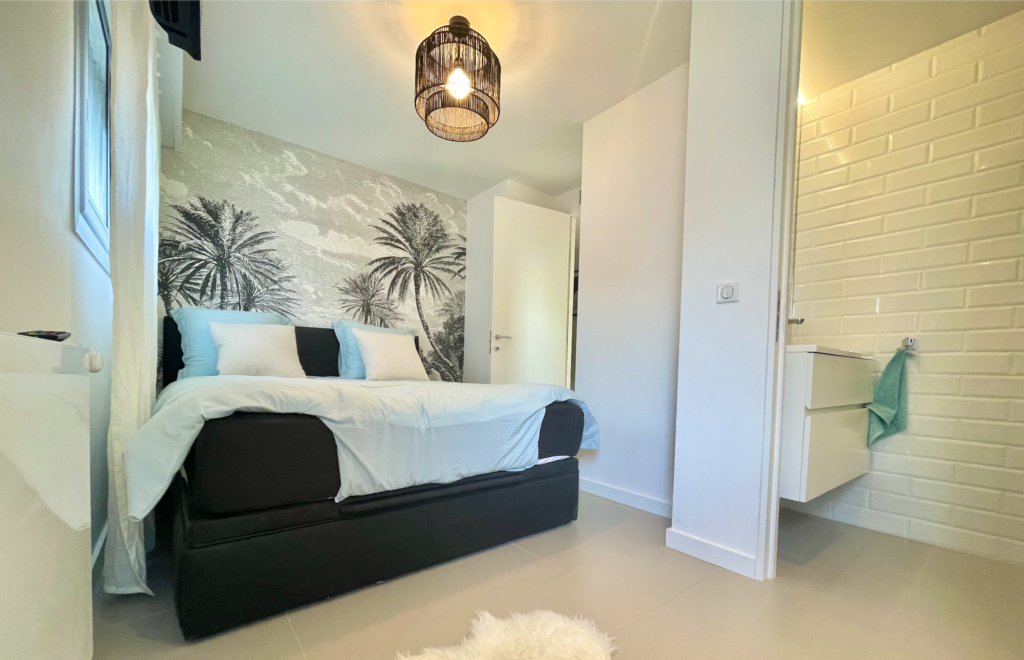 Aménagement intérieur d'un appartement de vacances cannois : chambre avec salle de bain avec une tapisserie murale sur-mesure avec comme motif central le palmier