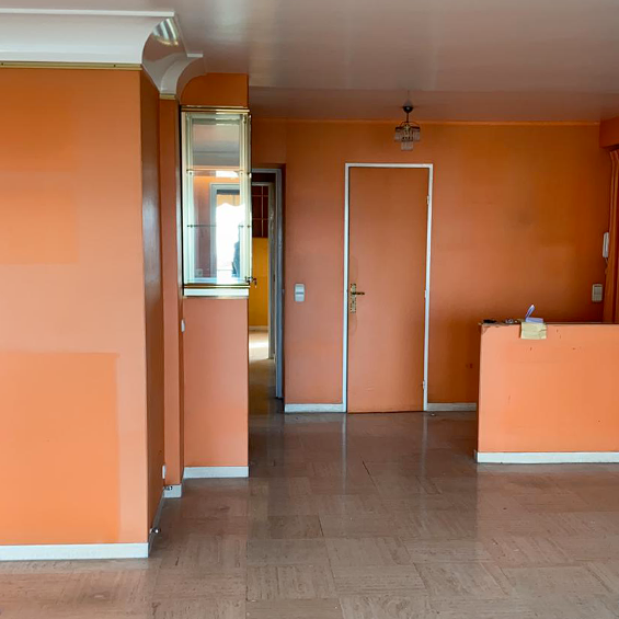 Aperçu de l'appartement cannois avant rénovation : entrée avec murs peints dans une teinte orange et un sol en travertin faisant écho à un style années 70