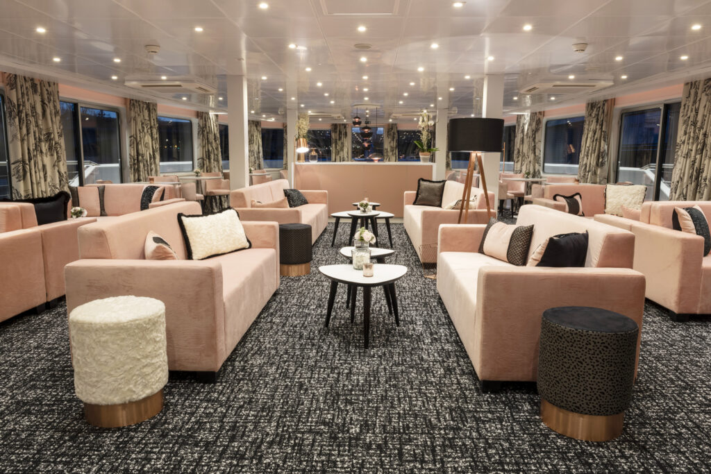 Agencement des espaces commun du bateau : salle lounge avec des teintes douces et élégantes (rose poudré, noir mat, cuivre)